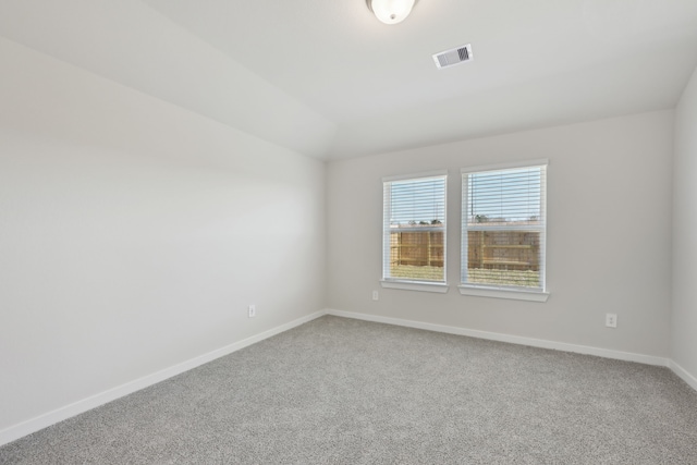 empty room featuring lofted ceiling, carpet floors, visible vents, and baseboards