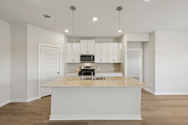 kitchen featuring stainless steel appliances, a sink, white cabinetry, an island with sink, and pendant lighting