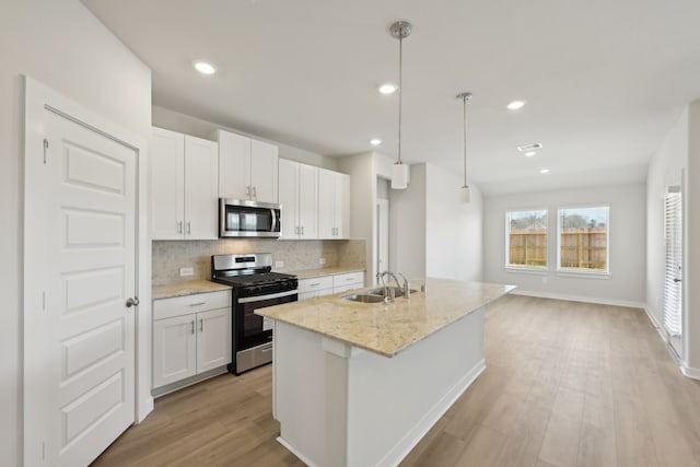 kitchen with a center island with sink, hanging light fixtures, appliances with stainless steel finishes, white cabinetry, and a sink