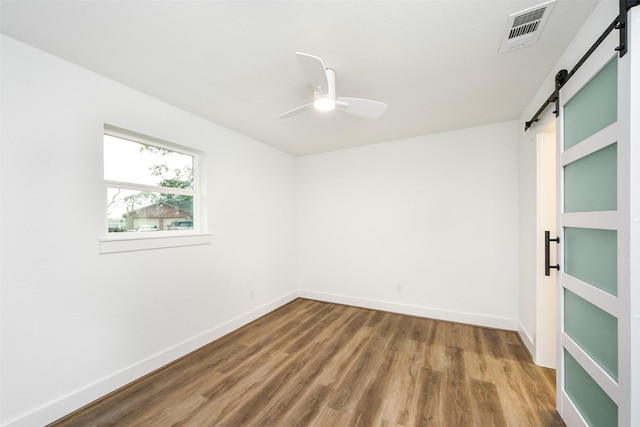 empty room featuring ceiling fan, wood-type flooring, and a barn door