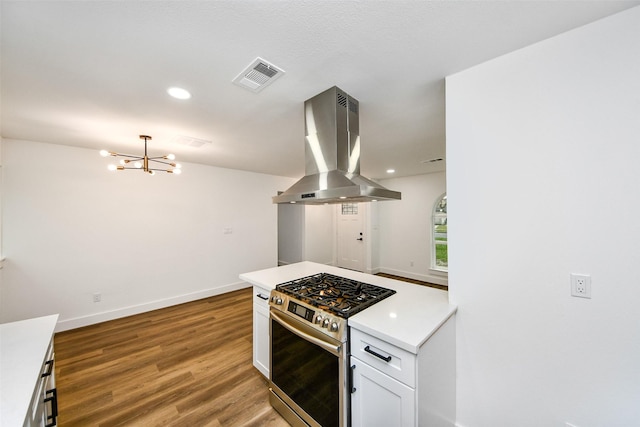 kitchen with island range hood, wood-type flooring, white cabinets, a chandelier, and stainless steel range with gas stovetop