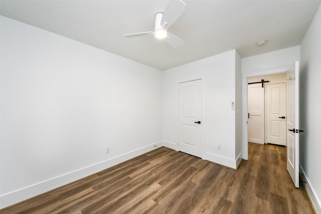 unfurnished bedroom featuring dark hardwood / wood-style floors, a barn door, and ceiling fan