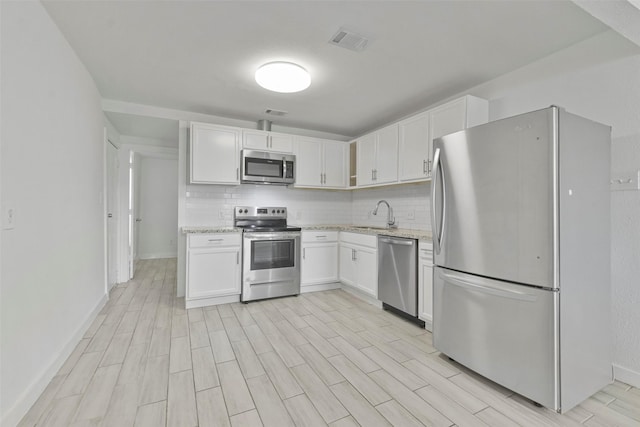 kitchen featuring white cabinets, sink, decorative backsplash, appliances with stainless steel finishes, and light stone counters