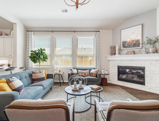 living room with a stone fireplace, a chandelier, lofted ceiling, and hardwood / wood-style flooring