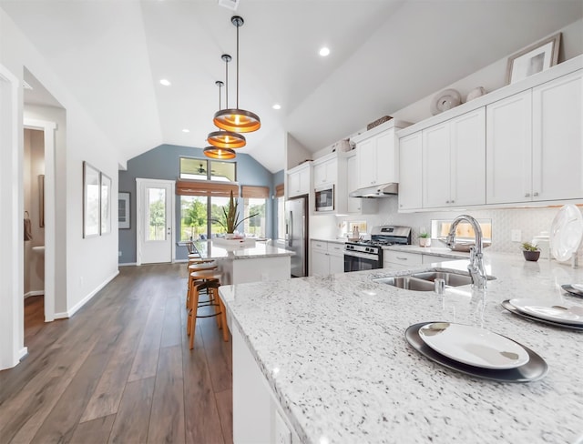 kitchen featuring light stone countertops, stainless steel appliances, pendant lighting, white cabinetry, and lofted ceiling