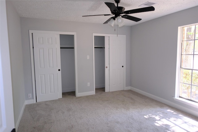 unfurnished bedroom with multiple windows, light colored carpet, ceiling fan, and multiple closets