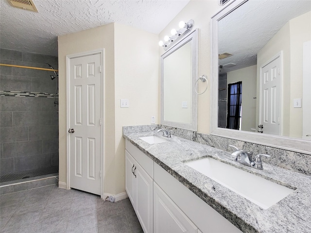 bathroom featuring tiled shower, vanity, a textured ceiling, and tile patterned flooring