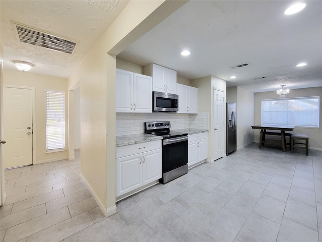 kitchen featuring backsplash, white cabinets, light stone counters, stainless steel appliances, and a chandelier