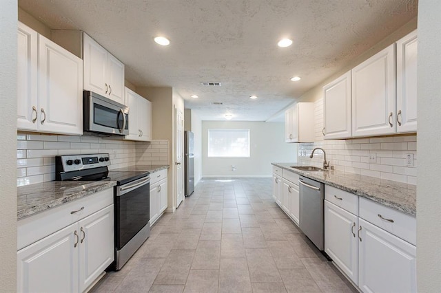 kitchen featuring sink, light tile patterned floors, light stone counters, white cabinets, and appliances with stainless steel finishes