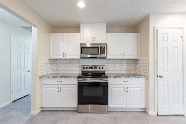 kitchen featuring white cabinets, light tile patterned flooring, light stone countertops, and appliances with stainless steel finishes