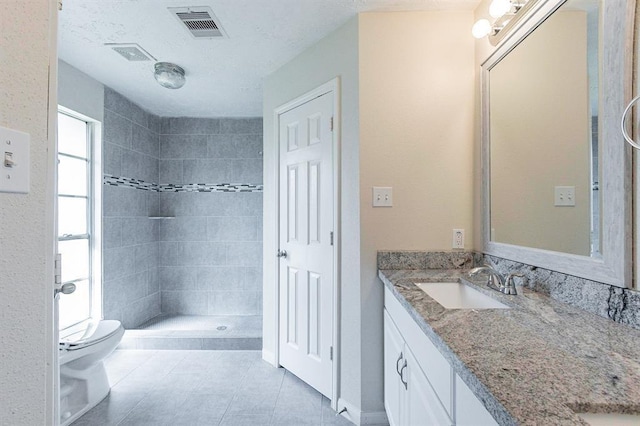 bathroom with tile patterned flooring, a tile shower, vanity, and toilet