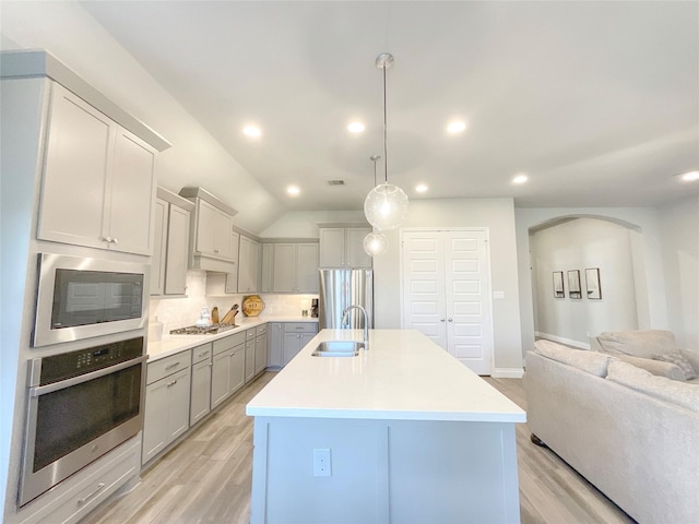 kitchen with lofted ceiling, a kitchen island with sink, hanging light fixtures, tasteful backsplash, and stainless steel appliances