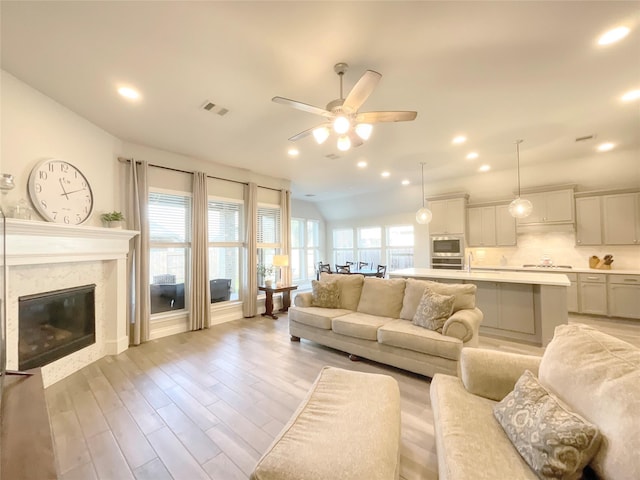 living room with ceiling fan, sink, a premium fireplace, vaulted ceiling, and light wood-type flooring