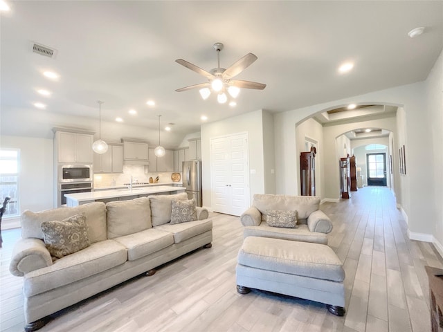 living room with ceiling fan, sink, and light wood-type flooring