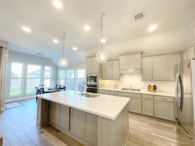 kitchen featuring sink, pendant lighting, vaulted ceiling, a kitchen island with sink, and appliances with stainless steel finishes