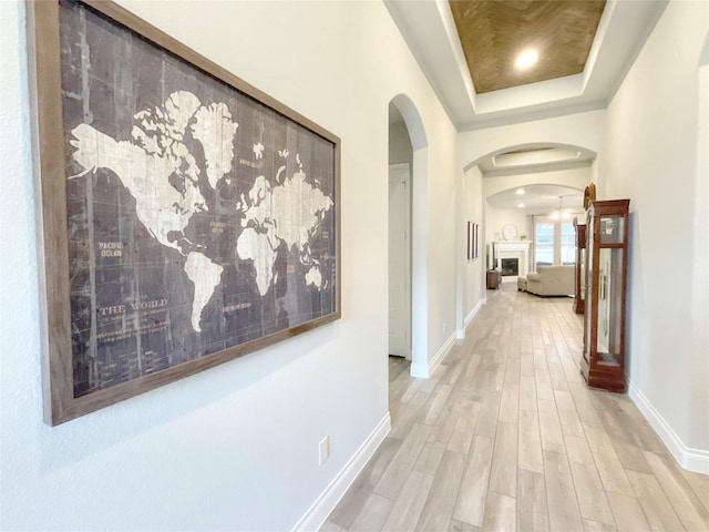 corridor with light hardwood / wood-style flooring and a tray ceiling