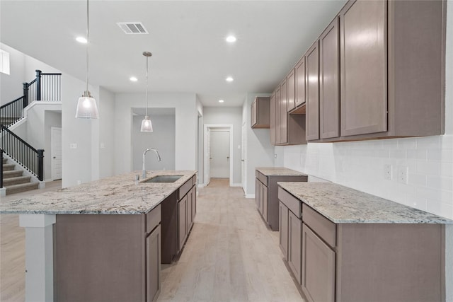 kitchen with decorative light fixtures, light stone counters, sink, and a kitchen island with sink