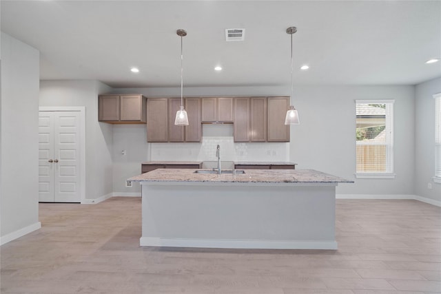 kitchen with light stone countertops, sink, pendant lighting, and a center island with sink