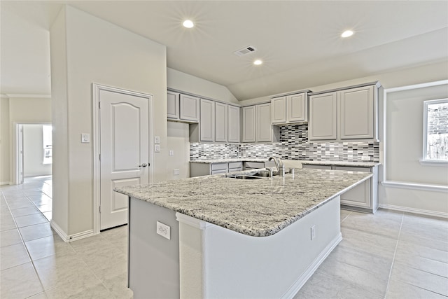 kitchen featuring light stone counters, an island with sink, a sink, and visible vents