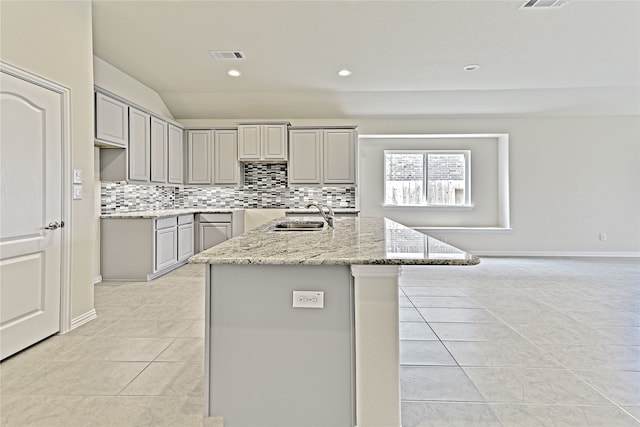 kitchen with light stone counters, gray cabinetry, sink, a center island with sink, and light tile patterned flooring