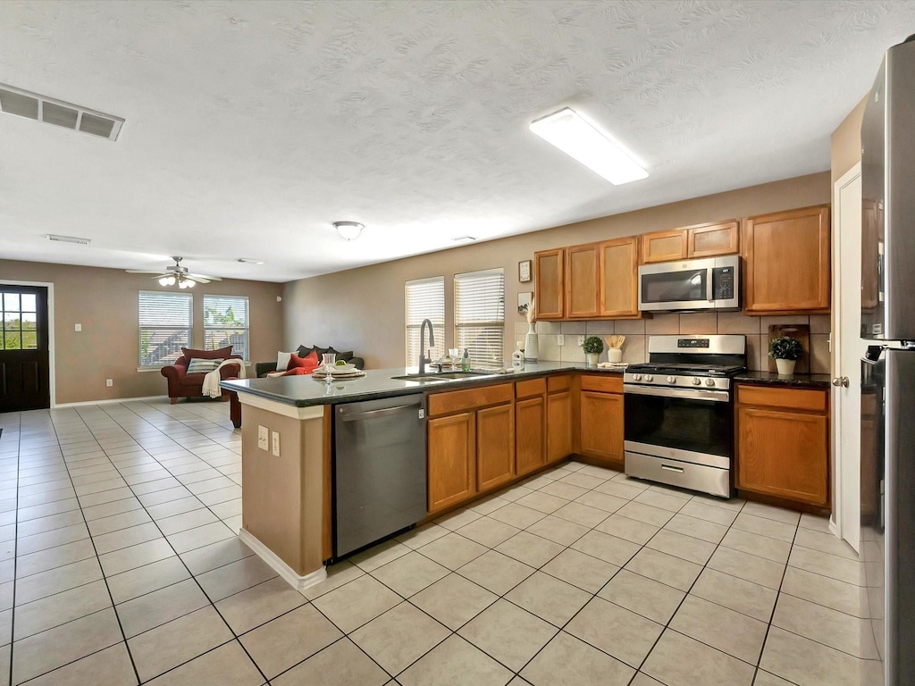 kitchen featuring sink, tasteful backsplash, light tile patterned flooring, kitchen peninsula, and stainless steel appliances