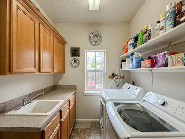 laundry area with cabinets, a textured ceiling, washer and clothes dryer, and sink