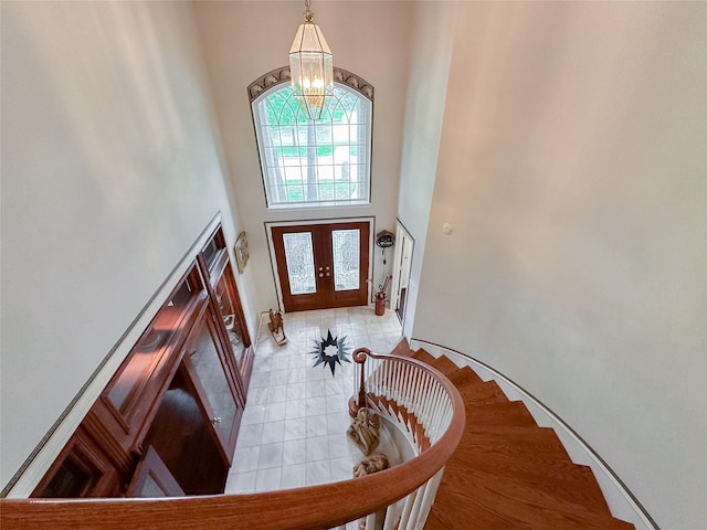 foyer entrance with french doors, light tile patterned flooring, a high ceiling, and an inviting chandelier