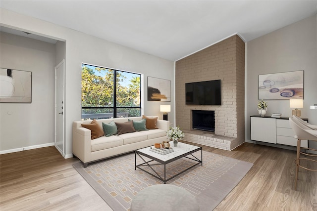 living room featuring light wood-type flooring, a brick fireplace, and vaulted ceiling