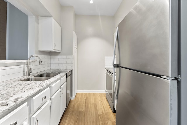 kitchen with sink, light wood-type flooring, appliances with stainless steel finishes, tasteful backsplash, and white cabinetry