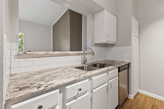 kitchen featuring light wood-type flooring, light stone counters, stainless steel dishwasher, sink, and white cabinetry