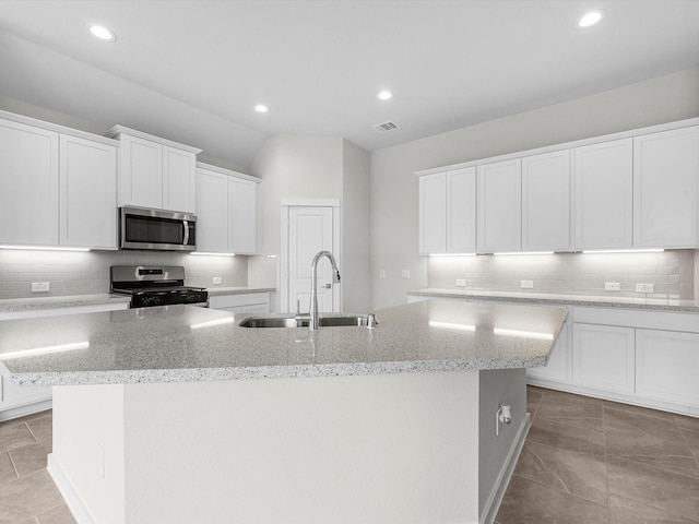 kitchen featuring light stone countertops, stainless steel appliances, a kitchen island with sink, sink, and white cabinetry