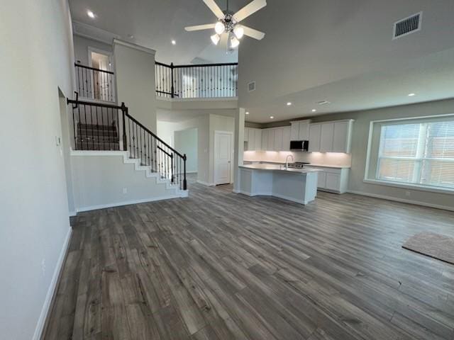 unfurnished living room with ceiling fan, sink, a high ceiling, and dark hardwood / wood-style floors