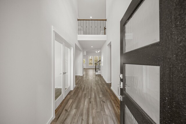 hall with wood finished floors, baseboards, and a towering ceiling