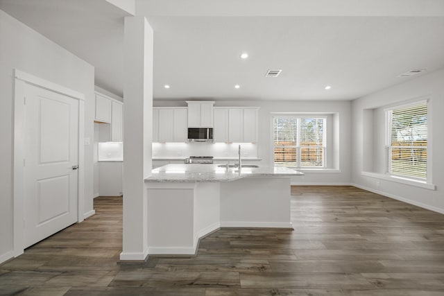 kitchen with a center island with sink, light stone countertops, white cabinets, dark hardwood / wood-style flooring, and sink