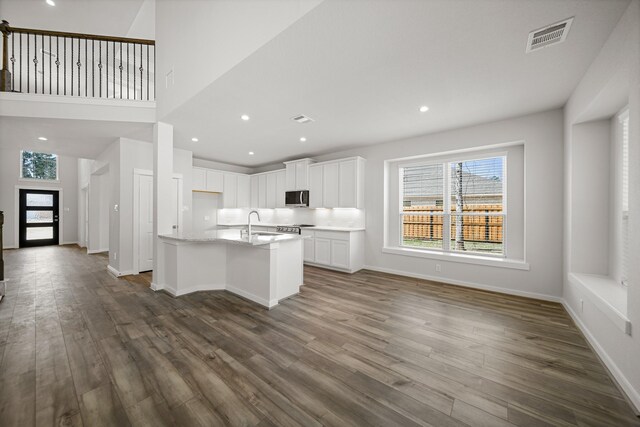 kitchen featuring plenty of natural light, an island with sink, white cabinets, and light stone counters