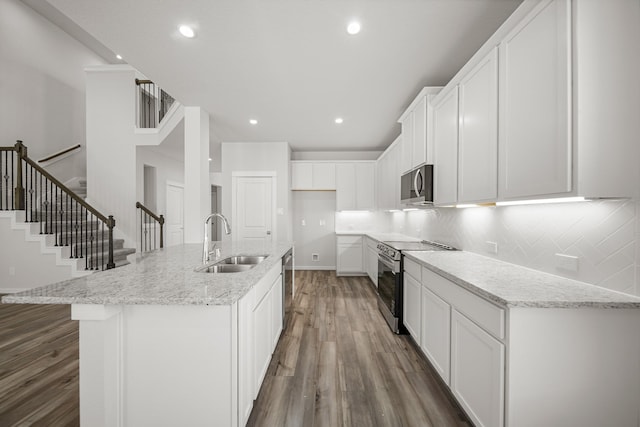 kitchen featuring appliances with stainless steel finishes, a center island with sink, light stone counters, white cabinets, and sink