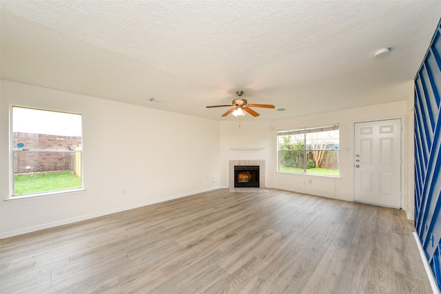 unfurnished living room with ceiling fan, light wood-type flooring, a textured ceiling, and a tile fireplace