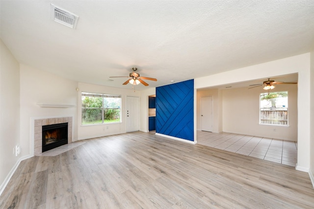 unfurnished living room featuring a fireplace, a textured ceiling, light wood-type flooring, and ceiling fan