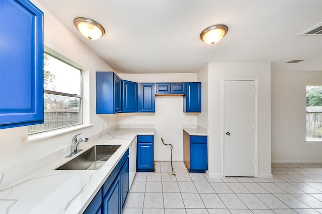 kitchen with blue cabinetry, light stone counters, sink, and light tile patterned floors