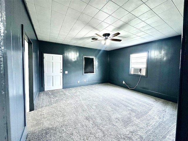 carpeted empty room with ceiling fan and wood walls