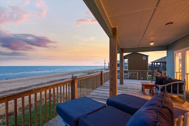 deck at dusk featuring an outdoor hangout area, a water view, and a beach view