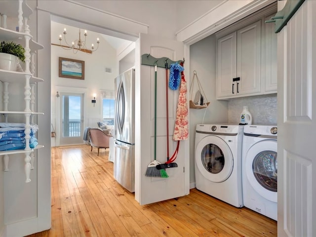 washroom featuring cabinets, light hardwood / wood-style floors, a notable chandelier, and washing machine and clothes dryer