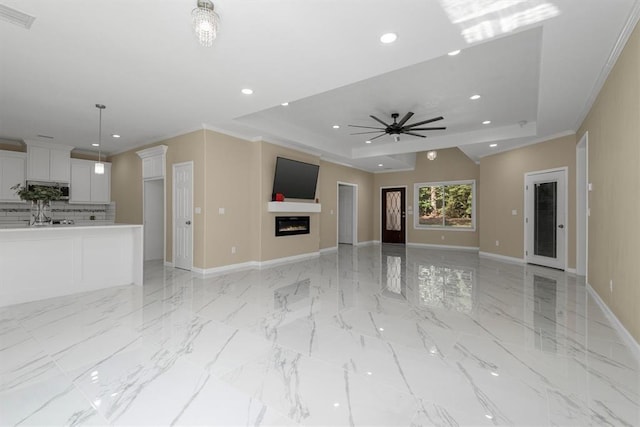 unfurnished living room featuring a raised ceiling, ceiling fan, and crown molding