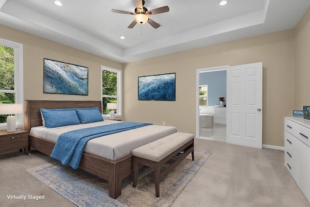 carpeted bedroom with a raised ceiling, connected bathroom, and ceiling fan