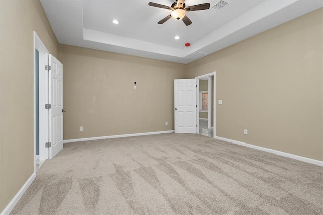 unfurnished bedroom featuring ceiling fan, a raised ceiling, and light carpet