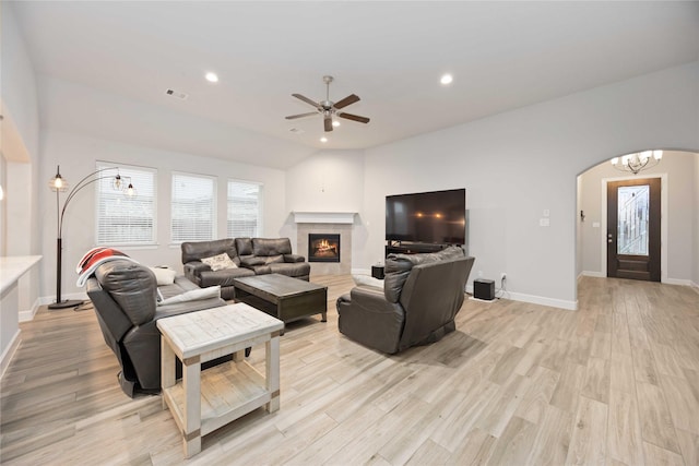 living room with ceiling fan with notable chandelier, a tiled fireplace, light hardwood / wood-style floors, and lofted ceiling