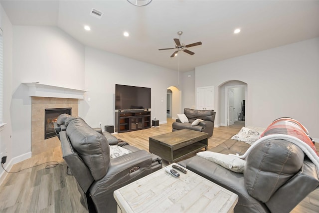 living room featuring ceiling fan, light hardwood / wood-style flooring, vaulted ceiling, and a tile fireplace