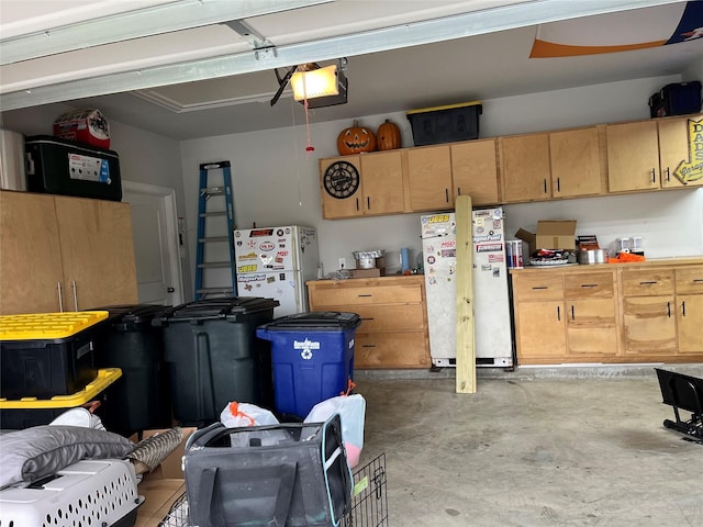 garage featuring refrigerator, white refrigerator, and a garage door opener