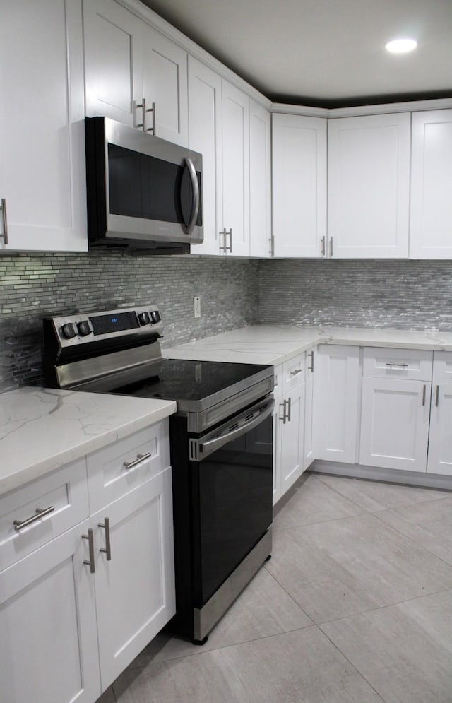 kitchen featuring light tile patterned floors, stainless steel appliances, white cabinetry, and light stone counters