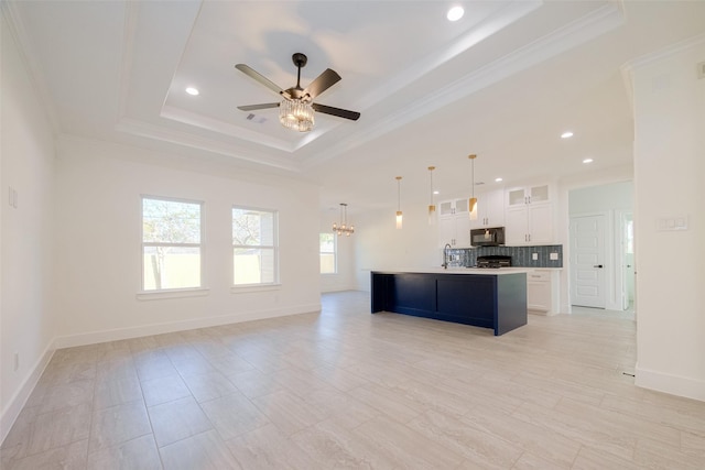 kitchen featuring ceiling fan with notable chandelier, a tray ceiling, decorative light fixtures, a center island with sink, and white cabinets